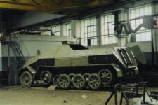 Niemiecki ciągnik opancerzony z czasów II wojny światowej. Pojazd stoi w hali remontowej.