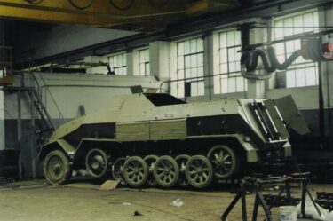Niemiecki ciągnik opancerzony z czasów II wojny światowej. Pojazd stoi w hali remontowej.