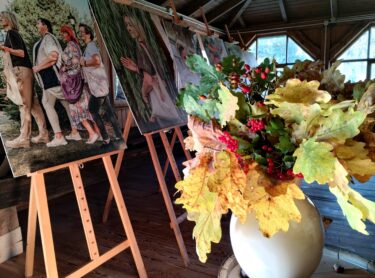 Wystawa fotografii umieszczonych na sztalugach w budynku ekspozycyjnym. Udekorowana jesiennymi liśćmi i roślinami.